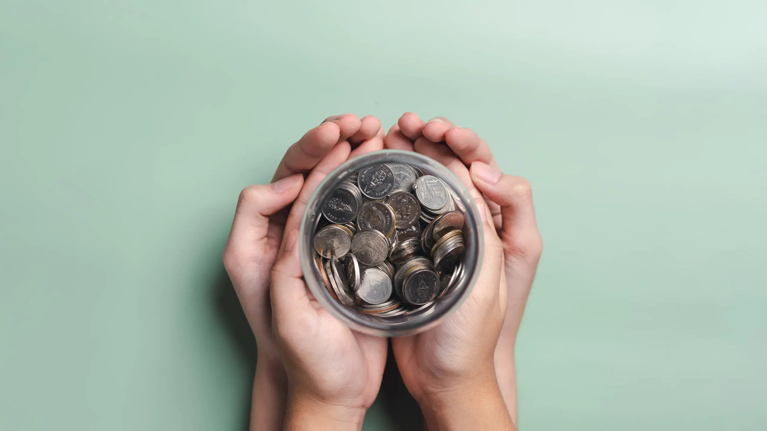 Hands holding a glass jar filled with coins